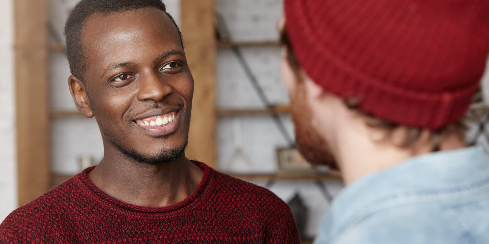 People, interracial friendship and communication concept. Handsome cheerful young Afro-American man dressed in cozy sweater smiling happily rejoicing at that his Caucasian friend got married People, interracial friendship and communication concept. Handsome cheerful young Afro-American man dressed in cozy sweater smiling happily rejoicing at that his Caucasian friend got married